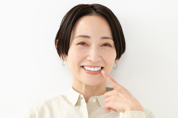 審美歯科治療で白く綺麗になった歯を指さして喜ぶ女性